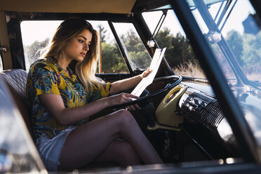 Junge Frau sitzt in einem Lieferwagen und liest eine Karte - KKAF01370