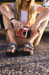 Junge Frau mit Oldtimer-Kamera sitzt draußen an einem Lieferwagen - KKAF01376