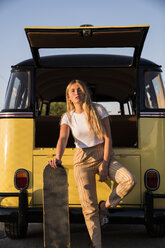 Young woman with skateboard standing outside at a vintage van - KKAF01378