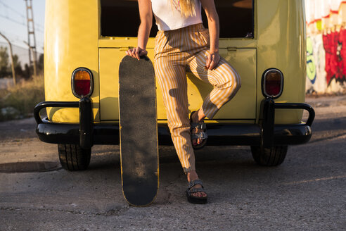 Junge Frau mit Skateboard steht draußen an einem alten Lieferwagen - KKAF01380