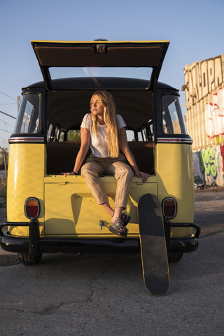 Junge Frau mit Skateboard in einem alten Lieferwagen sitzend, lizenzfreies Stockfoto