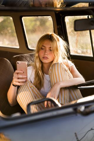 Junge Frau sitzt in einem Lieferwagen und benutzt ein Mobiltelefon, lizenzfreies Stockfoto