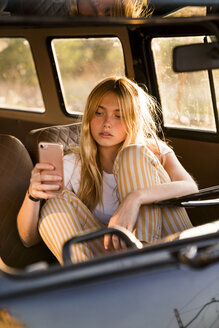 Junge Frau sitzt in einem Lieferwagen und benutzt ein Mobiltelefon - KKAF01390