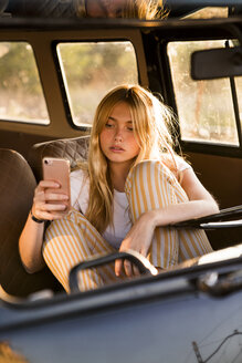 Young woman sitting in a van using cell phone - KKAF01390