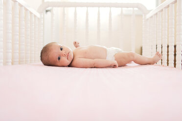 Baby wearing nappy lying on her back in a white crib. - MINF05068