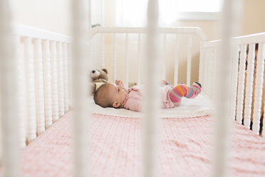 Baby wearing pink onesie lying on her back in a white crib. - MINF05069