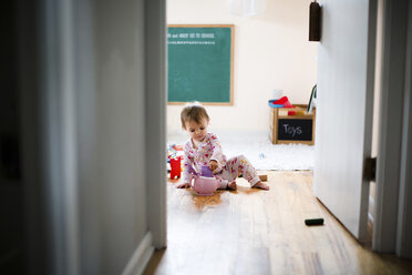 A toddler girl sitting on the floor playing with a toy tea set. - MINF05089