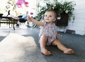 Baby girl sitting on house porch holding up a flower. - MINF05097