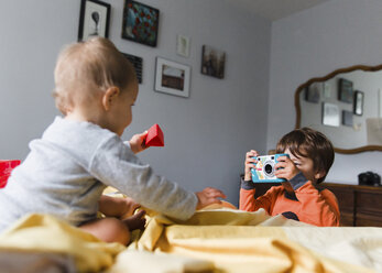 Junge, Kind fotografiert kleines Mädchen auf einem Bett sitzend. - MINF05104