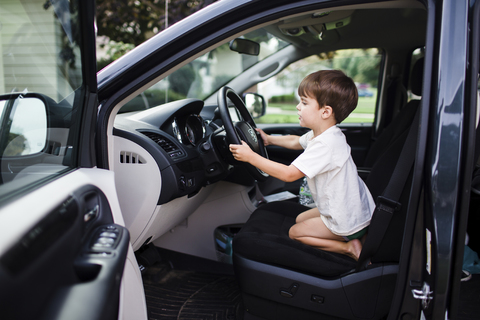 Junge, Kind kniend in einem Auto, das so tut, als würde es fahren., lizenzfreies Stockfoto