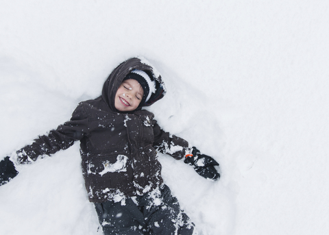 Junge, Kind liegend und spielend im Schnee., lizenzfreies Stockfoto