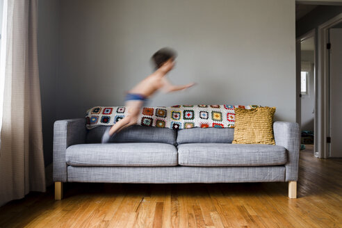 Junge, Kind springt auf einem Sofa im Wohnzimmer. - MINF05138