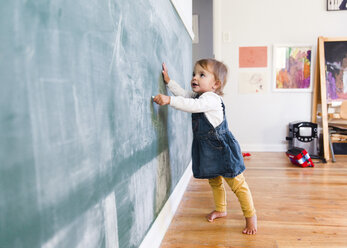 Ein Kleinkind, ein Mädchen, das mit Kreide auf eine Tafel zeichnet. - MINF05151