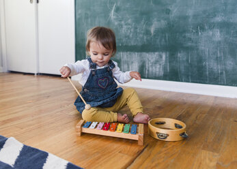 A toddler, girl playing with a xylophone in front of a blackboard. - MINF05152