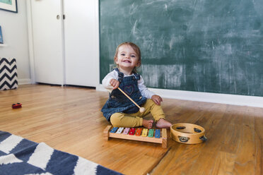 A toddler, girl playing with a xylophone in front of a blackboard. - MINF05153