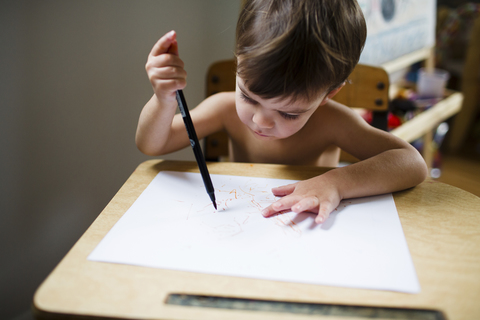 Blick von oben auf einen Jungen mit braunem Haar, der an einem Tisch sitzt, einen Stift hält und zeichnet., lizenzfreies Stockfoto