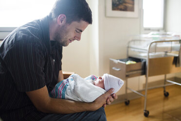 Man holding small baby wrapped in blanket, wearing hat. - MINF05188