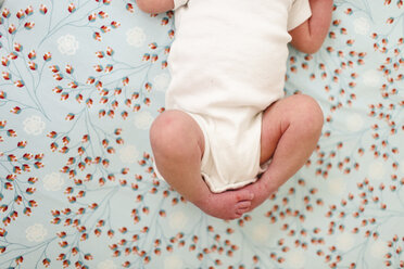 Blick von oben auf ein kleines Baby, das einen weißen Strampler trägt und auf dem Rücken liegt. - MINF05189