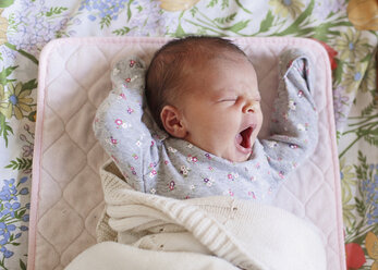 Blick von oben auf ein kleines Baby, das auf dem Rücken in einem Kinderbett liegt und gähnt. - MINF05192