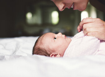 Nahaufnahme einer Frau, die sich über ein kleines, auf dem Rücken liegendes Baby beugt und die Hände des Babys hält. - MINF05194