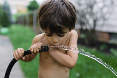 Close up of bare chested young boy with brown hair drinking water from a hose. - MINF05214