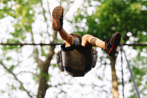 Low angle view of boy sitting on a swing underneath a tree. - MINF05215