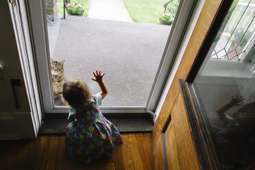 Hochformatige Rückansicht eines jungen Mädchens, das an einer Haustür kniet und das Glas berührt. - MINF05218
