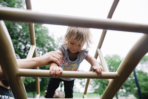 Nahaufnahme eines jungen Mädchens, das eine Leiter eines Klettergerüsts auf einem Spielplatz hochklettert. - MINF05220