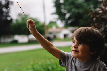 Nahaufnahme eines lächelnden Jungen mit braunem Haar, der eine Wunderkerze in die Höhe hält. - MINF05222