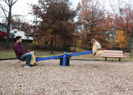 Mann und junges Mädchen sitzen auf einer Wippe auf einem Spielplatz. - MINF05240