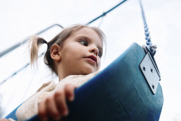 Low angle view of young girl with pigtails sitting on a swing. - MINF05241