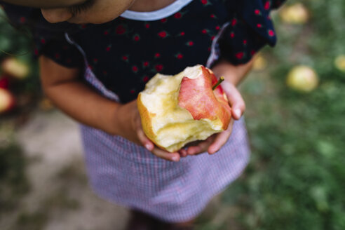 High angle close up of girl standing outdoors, holding half-eaten apple. - MINF05248