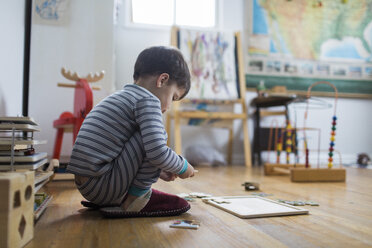 Junge, Kind, hockt auf dem Boden eines Spielzimmers und spielt mit einem Puzzle. - MINF05266