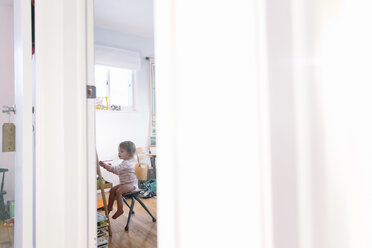 Blick durch eine offene Tür in ein Kinderzimmer, ein junges Mädchen sitzt auf einem Stuhl an einer Staffelei und zeichnet. - MINF05289