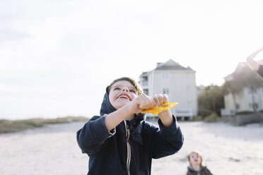 Lächelnder Junge an einem Sandstrand, der einen Drachen steigen lässt. - MINF05290