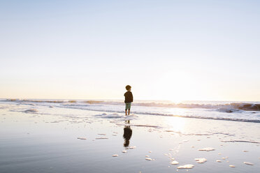 Young boy standing on a sandy beach by the ocean at sunset. - MINF05291