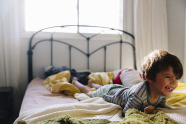 Lächelnder Junge mit braunem Haar, der auf dem Bauch auf einem Bett liegt. - MINF05295