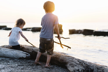 Junge und Mädchen spielen an einem Strand am Meer und halten Stöcke. - MINF05299