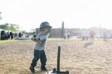 Young boy wearing baseball helmet standing on baseball field, holding baseball bat, hitting baseball. - MINF05300