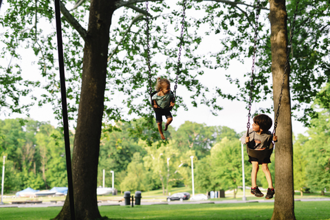Junge und Mädchen sitzen auf einer Schaukel unter Bäumen., lizenzfreies Stockfoto