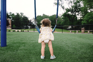 Rückansicht eines jungen Mädchens im Kleid, das sich auf einem Spielplatz an eine Schaukel lehnt. - MINF05302
