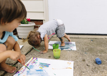 Young boy and girl outdoors on paving slabs, painting on canvasses. - MINF05310