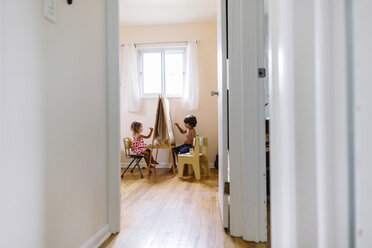 View through an open door into a nursery, boy and girl sitting on opposite sites of an easel, drawing. - MINF05318