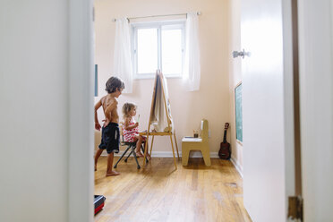 Blick durch eine offene Tür in ein Kinderzimmer, Junge und Mädchen an einer Staffelei, die zeichnen. - MINF05319