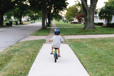 Rear view of young boy wearing crash helmet cycling along a pavement. - MINF05321