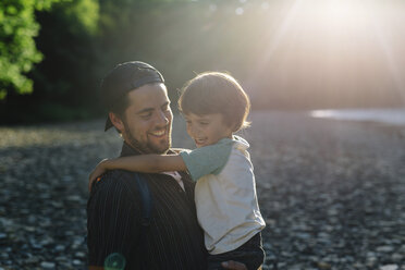 Smiling bearded man wearing baseball cap standing outdoors, holding young boy. - MINF05323