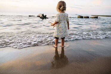 Rückansicht eines jungen Mädchens, das an einem Sandstrand steht und auf das Meer blickt. - MINF05328