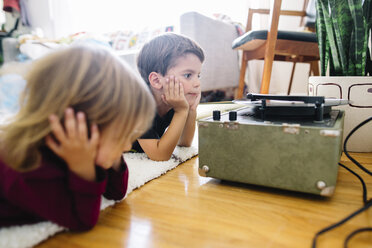 Ein Junge und ein Mädchen sitzen in einem Wohnzimmer auf dem Boden und schauen sich einen alten Plattenspieler an. - MINF05331