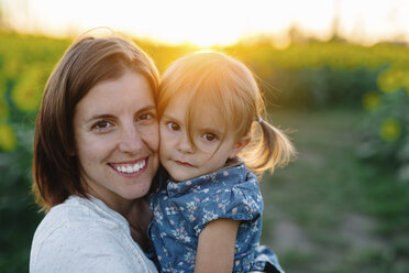 Smiling woman with brown hair standing outdoors, holding young girl with pigtails, looking at camera. - MINF05335