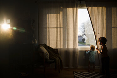 Zwei Kinder, ein Junge und ein kleines Mädchen, schauen aus dem Fenster. - MINF05348